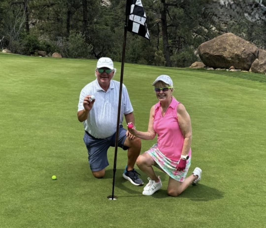 Two golfers kneeling beside the flag on a mountain course putting green