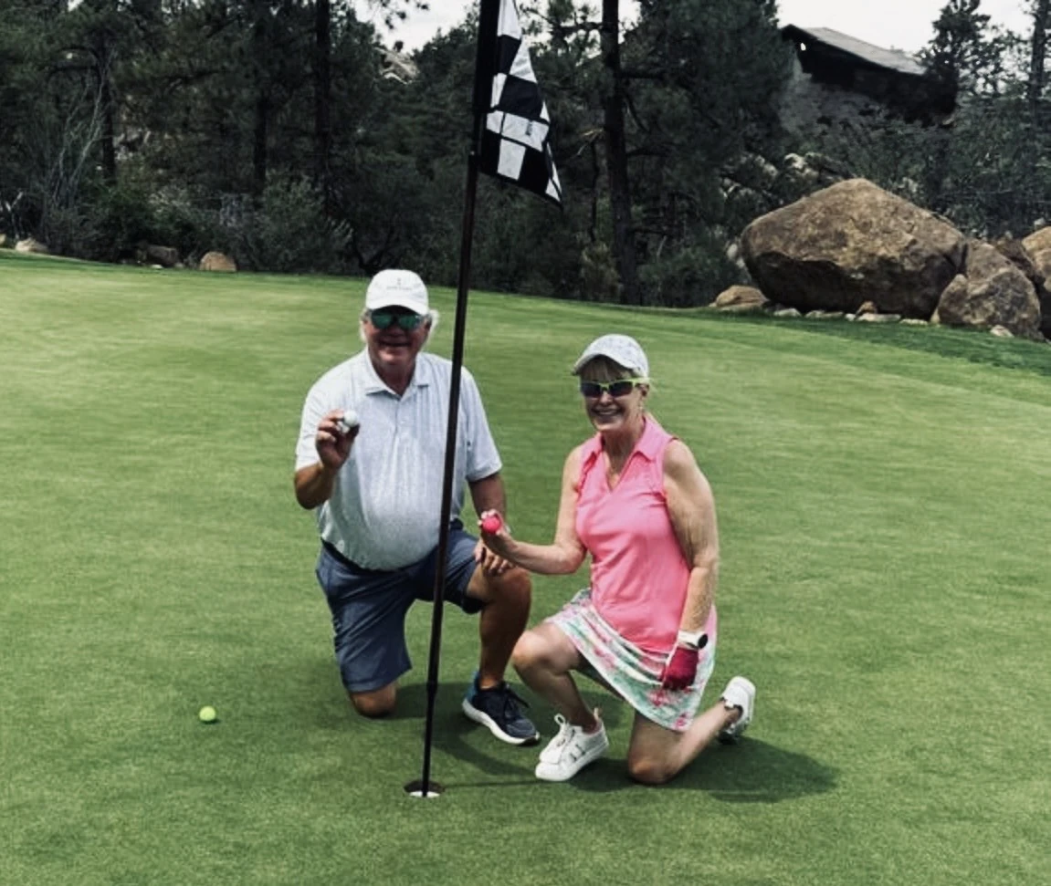 Two golfers smiling together beside the flag on a putting green